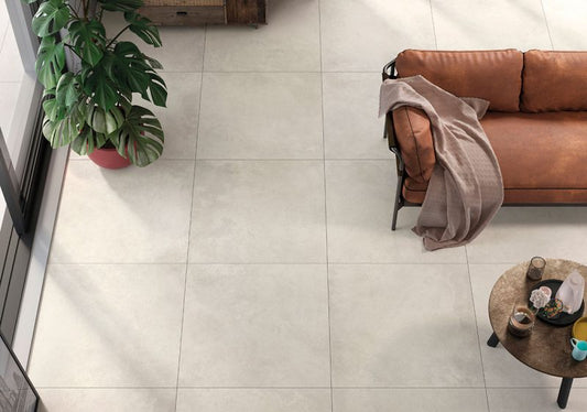 Ceramica Valsecchia Recover 'White', witgrijze betonlook vloertegels van bovenaf met een cognac leren bank en grote plant
