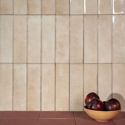 Estudio Cerámico Shallow 'Bone', beige glanzende wandtegels 6,4x22,3 staand verwerkt met een schaal pruimen op een rode vloer