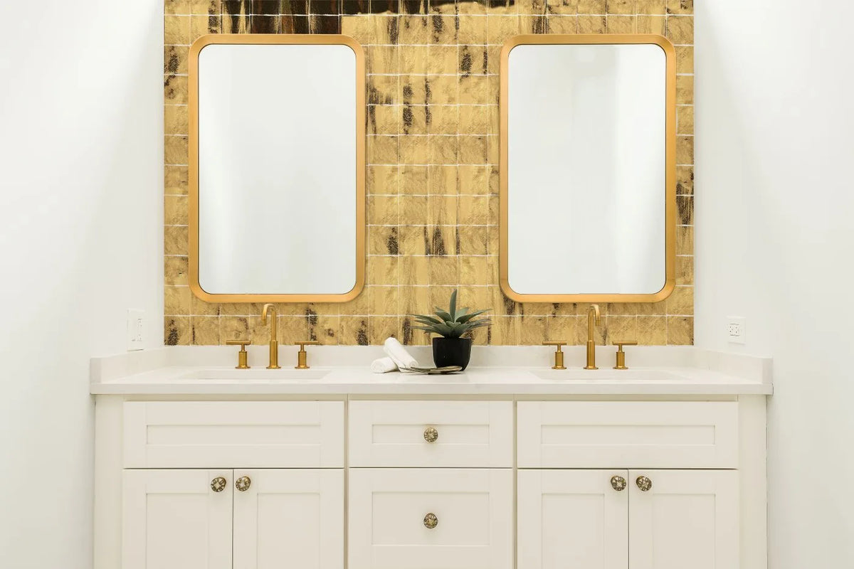 Tebe Vintage 'Gold', goudkleurige glanzende wandtegels achter een wit dubbel wastafelmeubel met twee spiegels